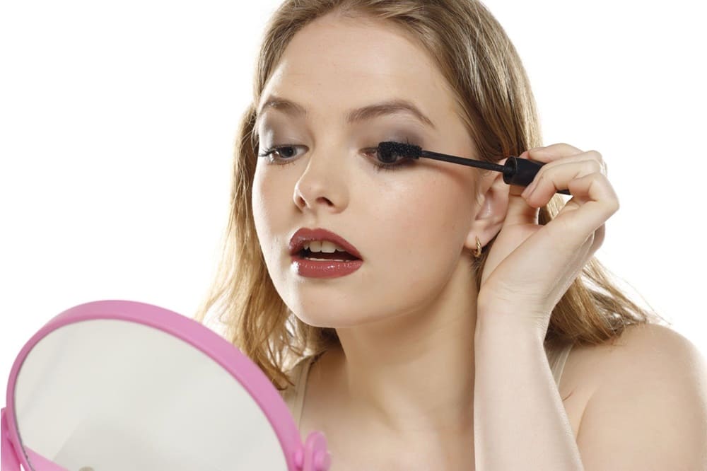 Young woman applying mascara on a white background