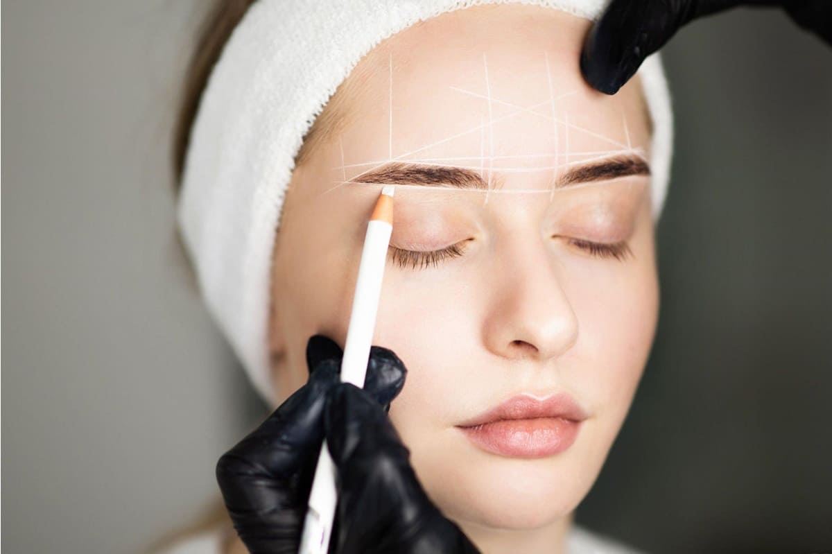 Cosmetologist Mapping Eyebrows Of Woman With White Pencil Before Permanent Makeup Treatment